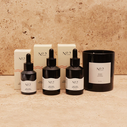 three black glass bottles of No.2 Co post poo toilet drops and a large black glass candle. Tile background